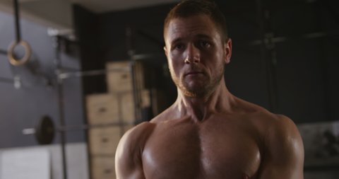 Front view close up of a shirtless athletic Caucasian man cross training at a gym swinging a kettlebell weight, slow motion