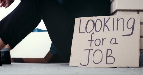 Fired depressed man sitting on ground next to carton banner saying looking for a job. Unemployed male office worker needs job. Unemployment rate. Financial crisis.
