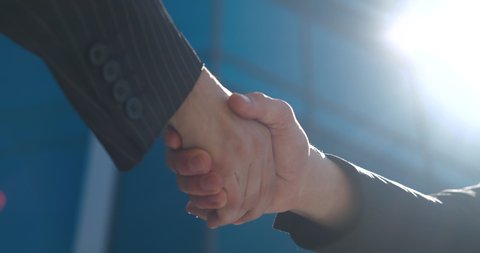 Closeup part of human body two men shake hands, conclude successful contract agreement, sign of support for partnership cooperation, businessmen in black jackets greet on street with male arms gesture