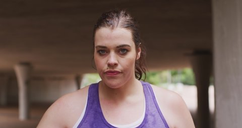 Portrait of curvy Caucasian woman with long dark hair wearing sports clothes exercising in a city, resting during her workout, in slow motion.