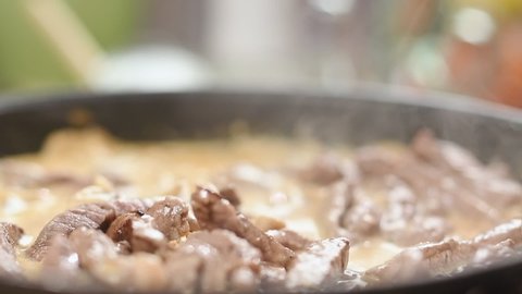 Chef stirring beef stroganoff in a frying pan.