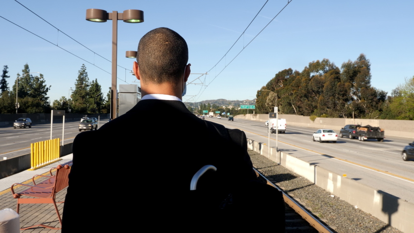 Businessman in a suit waits for a train while wearing a face mask to protect from getting sick