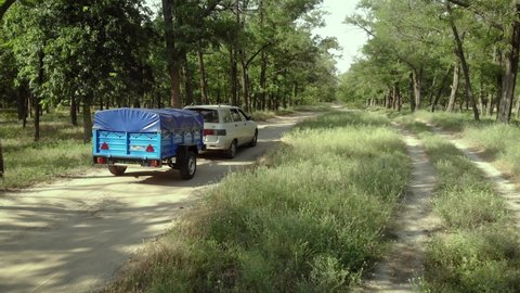 a passenger car with a light truck trailer moves along a coniferous forest road