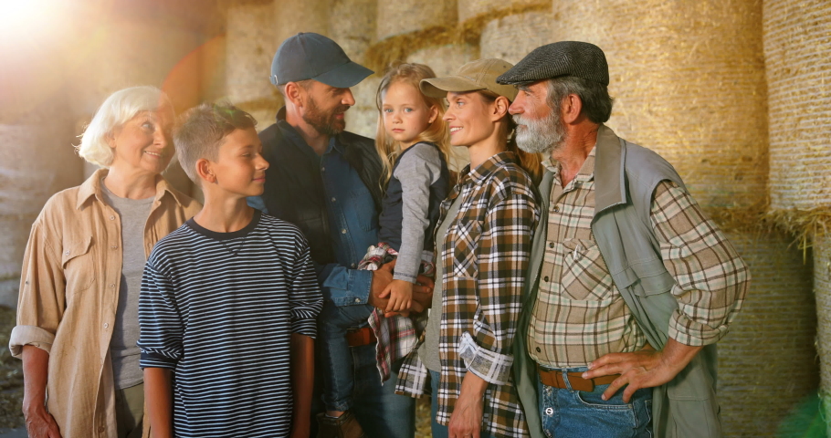 Portrait of happy Caucasian family of three generations standing outdoor at hay stocks and smiling to camera. Old parents with children and grandchildren in countryside. Farmers at farm. Summer. Royalty-Free Stock Footage #1058539186