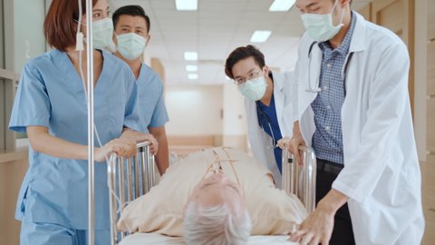 Group of Asian emergency doctor and nurse team wear face mask, push emergency stretcher, transport senior patient in hospital. Health care paramedic service, or medical rescue team operation concept