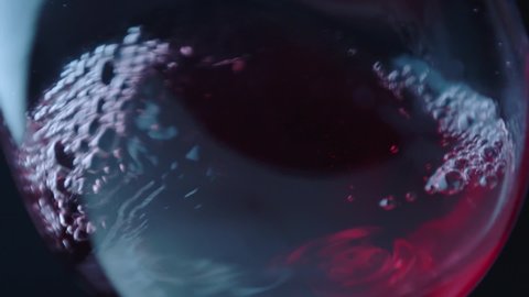 Waving red wine in a glass on defocused background . Beautiful stock footage for wine commercial . Close up video of wine mixing process inside goblet . Shot on ARRI ALEXA Camera in Slow Motion .