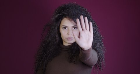Beautiful curly hair woman standing over red background with open hand doing stop sign with serious and confident expression, defense gesture. No more violence against women. Abuse. 4K.