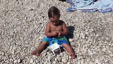 Stout child sitting and eating sweet cherries on the beach
