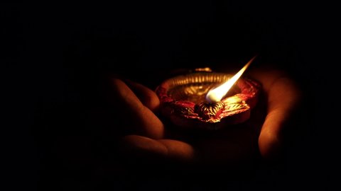 A person holding decorative colourful diya lamps lit during diwali festival. 