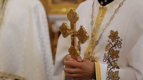 The priest holds a cross in his hands while standing in front of the parishioners.
