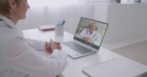online consultation of two medical specialists by video calling on laptops, woman is looking at male colleague at screen and listening