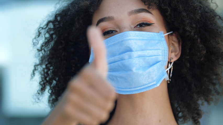 Beautiful smiling young african woman wrong puts on face mask to protect from coronavirus outbreak second wave of pandemic, looking at camera outdoor. Ethnicity student showing thumb up close up Royalty-Free Stock Footage #1058551351