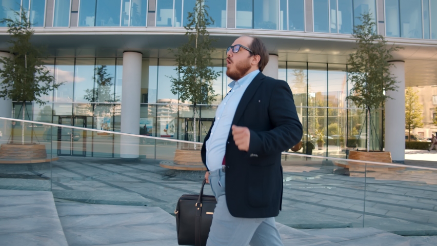 Joyful fat businessman dancing celebrating new career going to work outdoors. Funny overweight office manager dancing feeling happy about new startup project walking near business center Royalty-Free Stock Footage #1058557777
