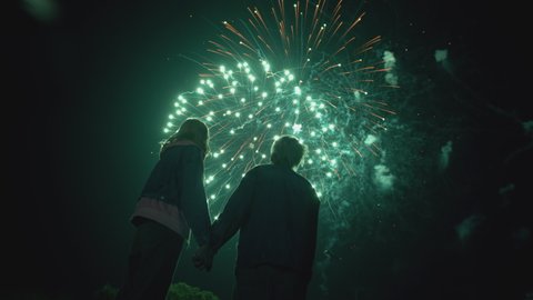 Young Couple Watching Beautiful Fireworks. Silhouette of people watching explosive and colorful fireworks in the evening sky. Holiday event and celebration. In slow motion