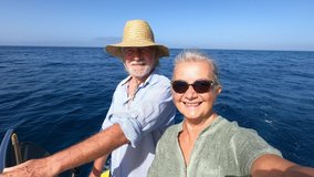 couple of cute mature people or senior enjoying and having fun together in the middle of the sea or ocean with a small boat or dinghy - woman pensioner taking a selfie with her old man driving the boa - Powered by Shutterstock - Get 15% off with code: PIKWIZARD15