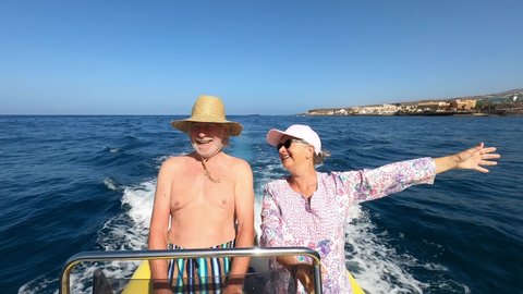couple of two senior and mature people having fun ad enjoying together their vacations with a rent boat of dinghy in the middle of the sea or ocean -happy seniors driving a small boat smiling 
