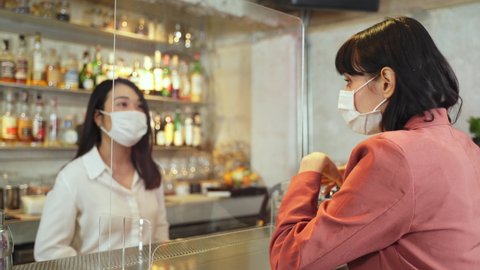 Customer woman dining in restaurant. Waitress with face mask serving food to customer sit on social distancing table for new normal lifestyle in restaurant after coronavirus or covid-19 pandemic.