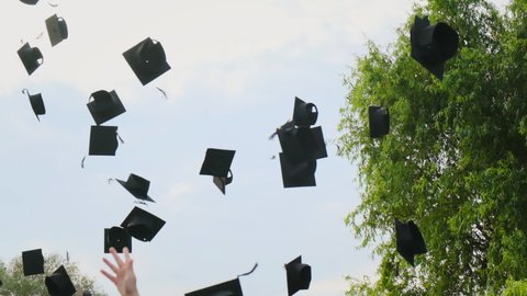 High school students graduate throwing graduation square academic cap bonnet into the sky in slow motion, education college ceremony in front of threes. Hands catching hats after finishing university