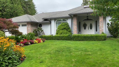 Establishing shot of one story brick and white stucco luxury house with garage door, big tree and nice landscape in Vancouver, Canada, North America. Day time on September 2020. Slow pan left. H.264.
