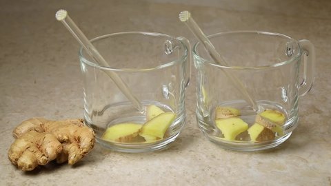 Pouring fresh hot organic ginger tea in glass cups and raw ginger root