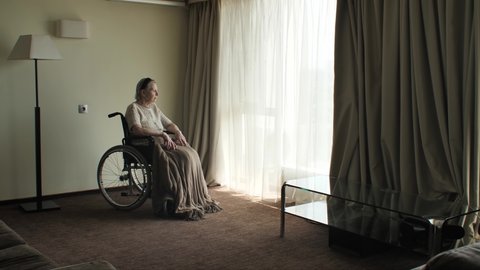 Senior woman sit on wheelchair and looks through the window