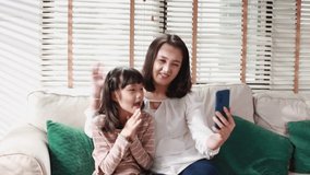 Asian family making a video call and waving at the caller with daughter in living room at home.