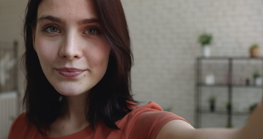 Beautiful lively 20s coquette woman holds smart phone recording video for social networks makes funny faces, dances moves flirting grimacing looking at camera, having fun alone at home, close up view