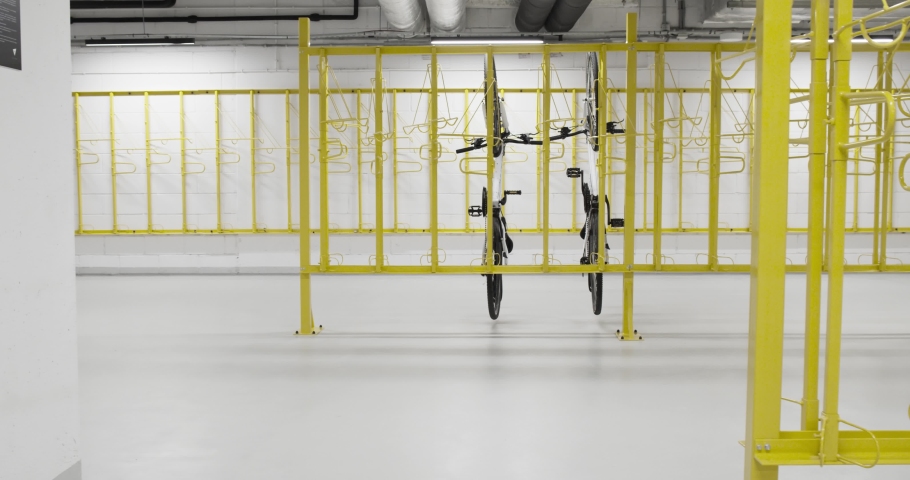Bicycle depot in modern office or residential comples. Bike storage room interior with yellow stands and hanging racks. New, white, clean floor. Parking for bicycles. Royalty-Free Stock Footage #1058571532