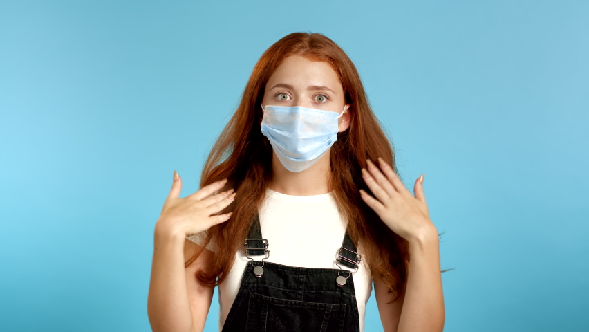 Young tired woman in protective mask is dissatisfied, unhappy.  she exhales from heat or stuffiness, waves arms at herself. Heatstroke concept. | Shutterstock HD Video #1058572255