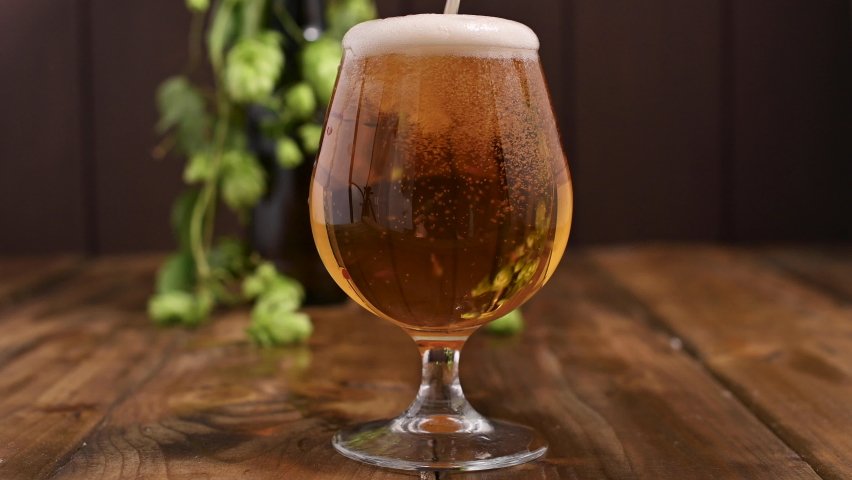 Beer. Cold Craft light Beer in a glass with water drops. Pint of Beer close up on a wooden background. Beer is pouring from the bottle. Border design. High quality 4k footage | Shutterstock HD Video #1058572513