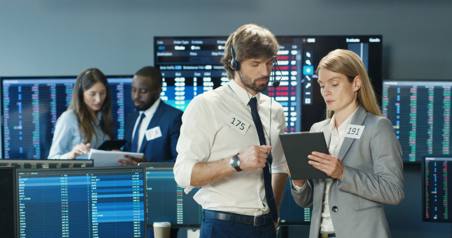 Caucasian male female couple of trading co-workers talking, selling or buying stocks with tablet device. Man and woman, traders looking at gadget with numbers. Colleagues discussion at exchange market Royalty-Free Stock Footage #1058573923