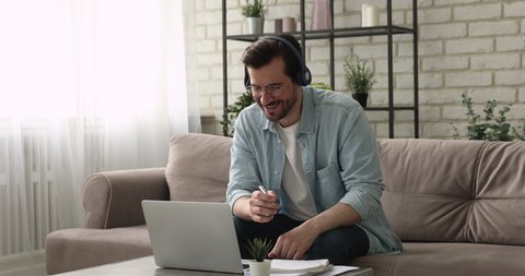 Businessman sit on sofa talk with client solve issues distantly through wireless headphones, writing information in copybook. E-learn with e tutor, improve knowledge use videocall, modern tech concept