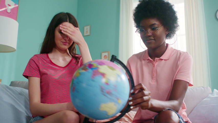 Young women, best friends, travelers, have fun playing with globe, trying to guess next travel destinations, have great planning time at home, happy and excited, Foreground, Slow motion.