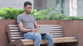 Cheerful Young African Man doing Video Call on Laptop on Bench 