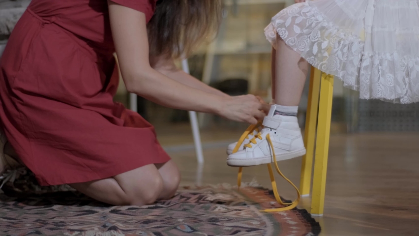 Mother ties her daughter's shoes.Mother ties laces of her daughter's sneakers. The mother's hands tie shoelaces to the legs of the child wearing shoes. Childcare and motherhood concept.Close-up. Royalty-Free Stock Footage #1058577061