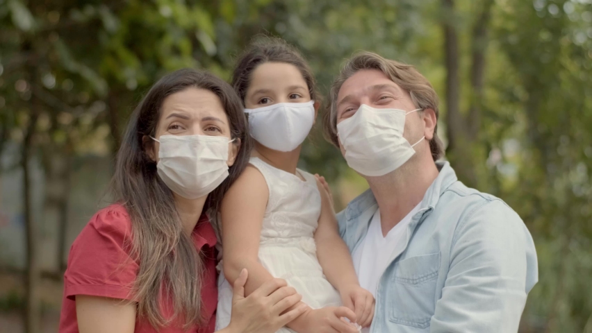 The young family hugs each other and looks away. They point each other in the distance and wear medical masks to protect them from the virus. Royalty-Free Stock Footage #1058577205