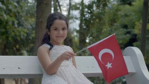 Small girl smiles to the camera in the park and waving the flag of Turkey.Slow motion video.