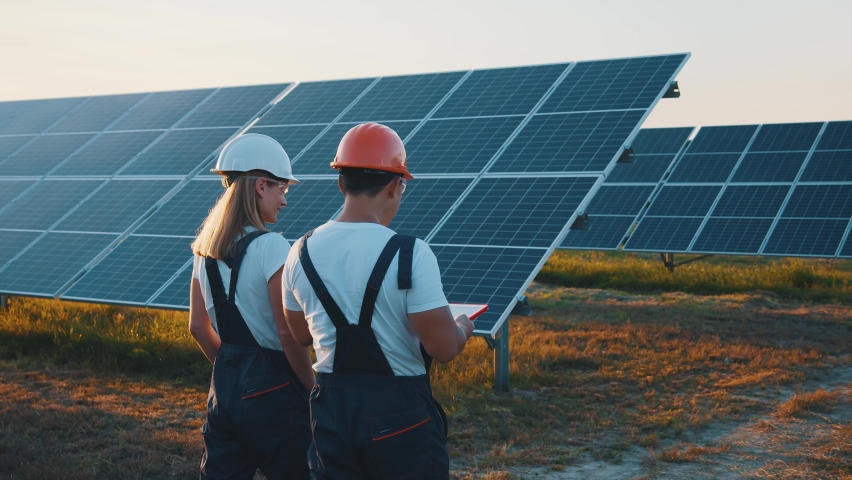 Interracial team of industrial colleagues using tablet monitoring rows of photovoltaic solar panels at sunset. Business cooperation. Solar park. Alternative energy concept. | Shutterstock HD Video #1058579977