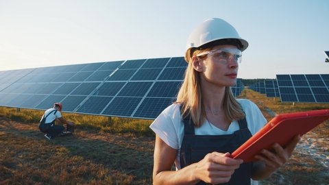 Female ecological engineer uses digital tablet and collects efficient information about solar panels. Photovoltaic solar farm. Green energy. Environment.