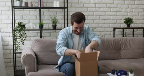 Man sit on couch opening carton parcel box feels satisfied by goods delivered from on-line webshop store. E-shopping e-commerce buyer, trusted transporting company fragile items are in order concept