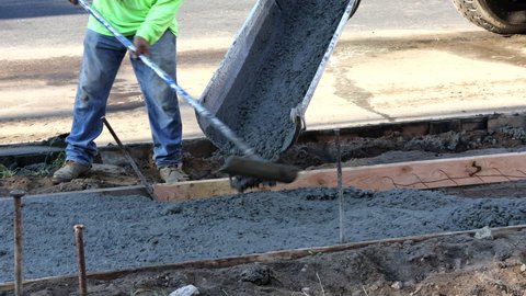 Labour builders at construction site filling formwork with cement workmen in the process of forming new sidewalk concrete