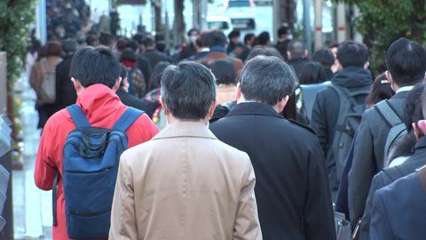 TOKYO, JAPAN -MAR 2020 : Back shot of unidentified crowd of people walking down the street in busy rush hour. Many commuters going to work. Japanese business man and woman, job and lifestyle concept.