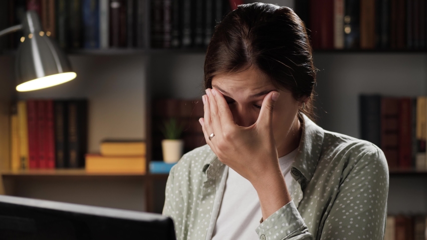 Eye fatigue. Tired woman at workplace in evening works at laptop, girl touches her head and eyes. Manager syndrome, insomnia concept | Shutterstock HD Video #1058584804