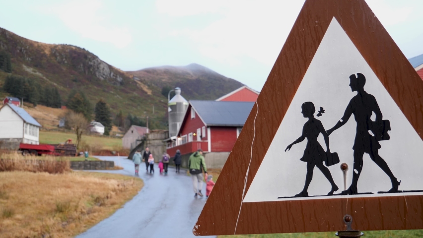 School children crossing sign in a picturesque, rural community with children walking home with parents in the background - static