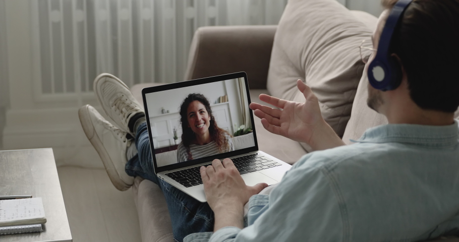Relaxed man resting on couch wearing headphones talking with woman use videocall app, pc screen view over male shoulder. Couple in separation long distance relationship, video conference usage concept | Shutterstock HD Video #1058587930