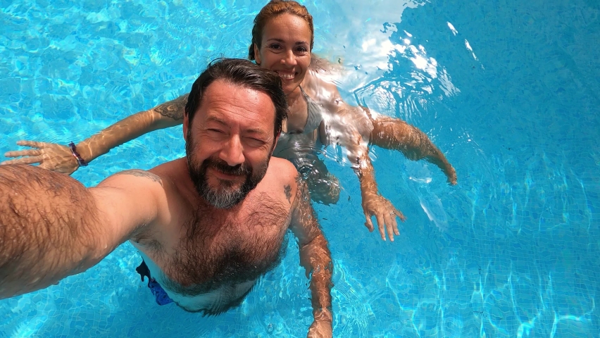 Happy caucasian people couple have fun and enjoy the swimming activity at the pool - concept of holiday summer vacation in resort or hotel - cheerful  adult man and woman together