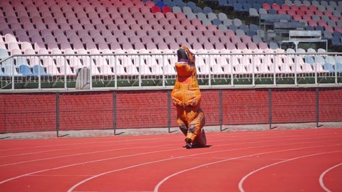 Big dragon in blow-up costume. Person dressed in funny orange costume walks on stadium in a sunny day.