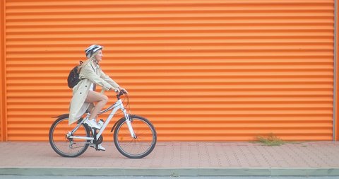 Woman bicyclist in helmet riding on orange background in the city on sport retro bike. 4K video. 