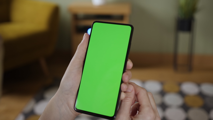 Young Woman Home Sitting on a Couch with Green Screen Smartphone in Vertical Mode. Girl Using Touch Screen Mobile Phone. Girl Using Smartphone, Browsing Internet, Watching Video Content, Blogs. POV. | Shutterstock HD Video #1058602366