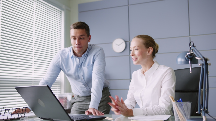 young man and woman work together in office with laptop on desk. make high five, succesful teamwork. looks positive and cheerful, smiles. 
